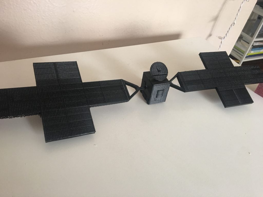 This image shows a small 3D model of the Psyche spacecraft that was printed in black PLA plastic. It is approximately 18 inches long, 5 inches wide, and 2 inches high.