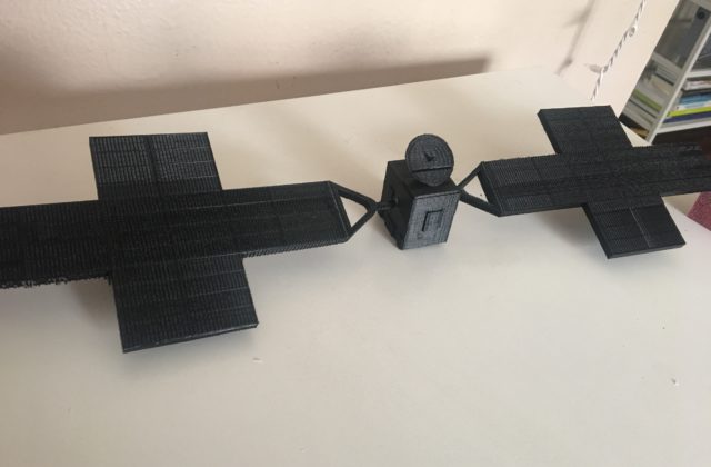 This image shows a small 3D model of the Psyche spacecraft that was printed in black PLA plastic. It is approximately 18 inches long, 5 inches wide, and 2 inches high.