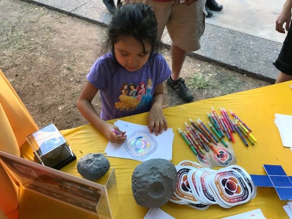 This image shows a young child intently coloring in the Psyche badge.