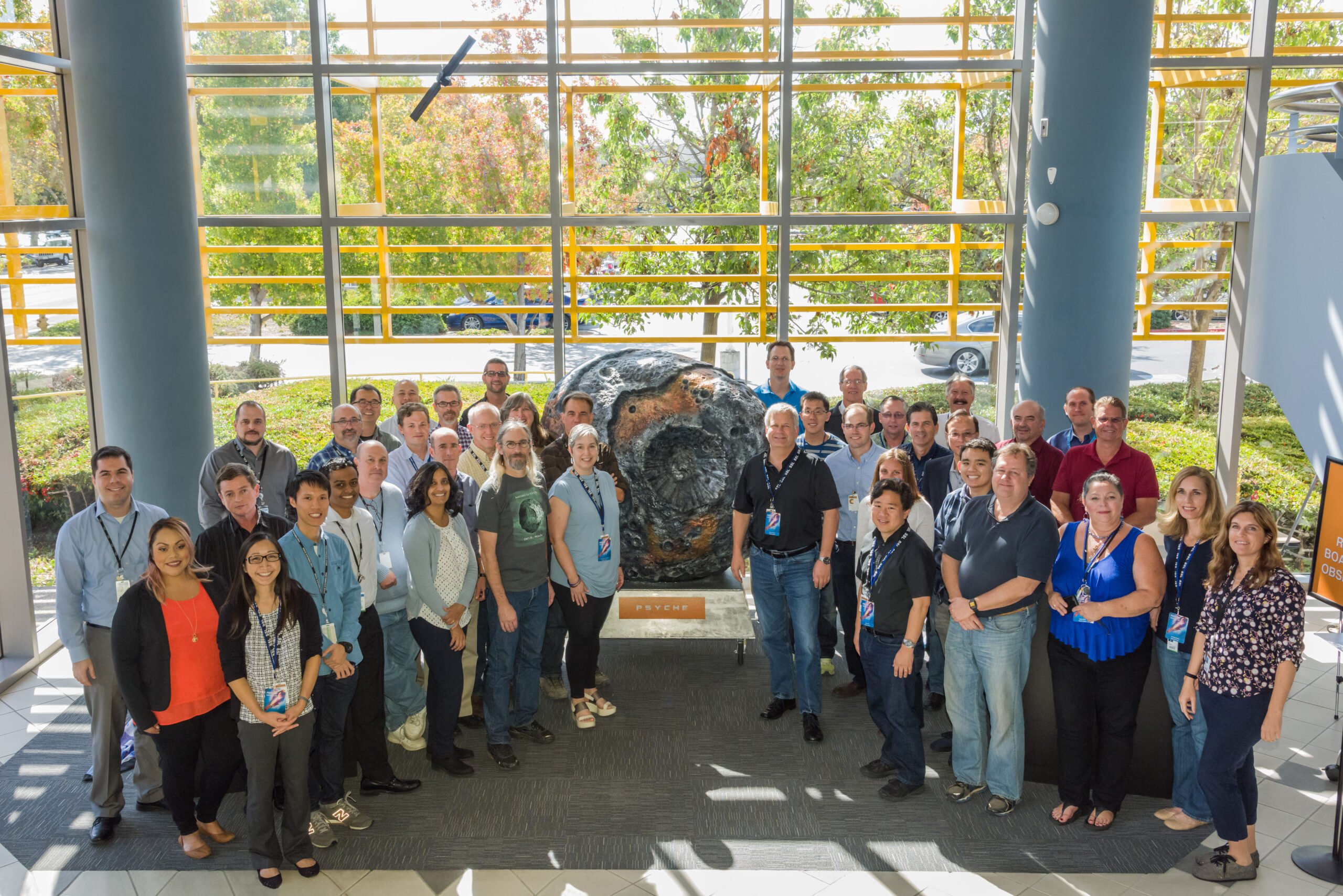 This is a photograph of members of the Psyche team standing in front of a 3D mid size Psyche model located within the Maxar (formerly SSL) facility.