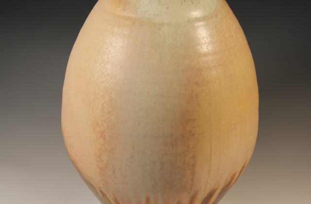 This image shows an oval ceramic vessel with a lid. The glaze is a mix of tans, dark reds, and browns with streaks that are prominent near the base. The lid has a textured knob on top.