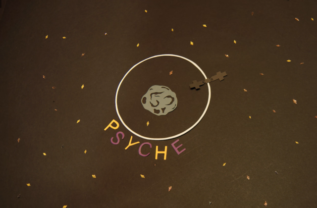 This image shows a frame of the Psyche Stop Motion video. In this frame, the Psyche spacecraft is orbiting the Psyche asteroid and the words Psyche are shown.