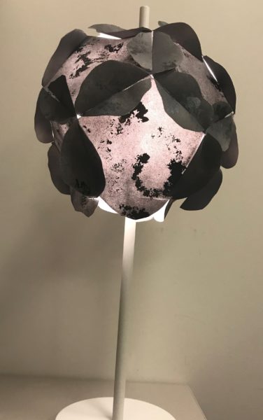 This image shows a table lamp with a custom shade made of grey painted and speckled paper in the shape of the Psyche asteroid.