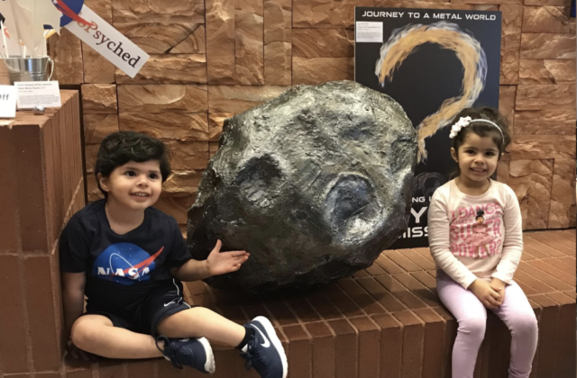 Two kids take a picture next to the fake psyche asteroid.