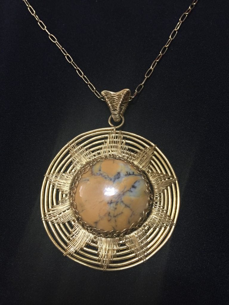 Circular pendant made from orange dendritic opal wrapped with brass wire, in a pattern shaped like the sun.