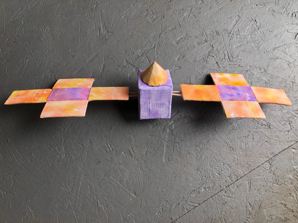 A handmade purple and orange psyche spacecraft constructed of cardboard, papier-mâché, flour sack towels, and watercolor.