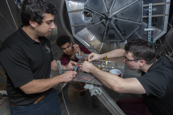 Undergraduate students working on their prototype in a large vacuum chamber.