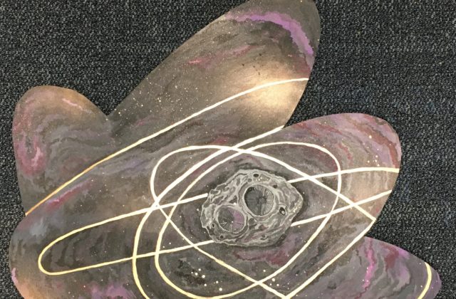 This piece shows trajectory lines framing Psyche. The project highlights the asteroid and shows the Psyche orbiter dancing with the space object. Black, purple and pink clouds were painted with rosy golds to create visual interest. Psyche is painted in the middle towards the right with rings of gold around it, signifying paths the Psyche orbiter might take. Spray paint gold was used to make speckled stars and clouds of gold in the background.