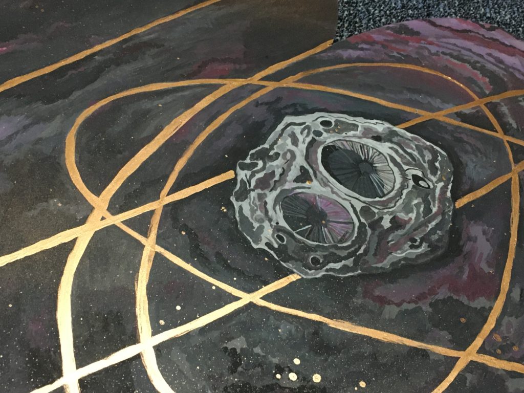 This piece shows trajectory lines framing Psyche. The project highlights the asteroid and shows the Psyche orbiter dancing with the space object. Black, purple and pink clouds were painted with rosy golds to create visual interest. Psyche is painted in the middle towards the right with rings of gold around it, signifying paths the Psyche orbiter might take. Spray paint gold was used to make speckled stars and clouds of gold in the background.