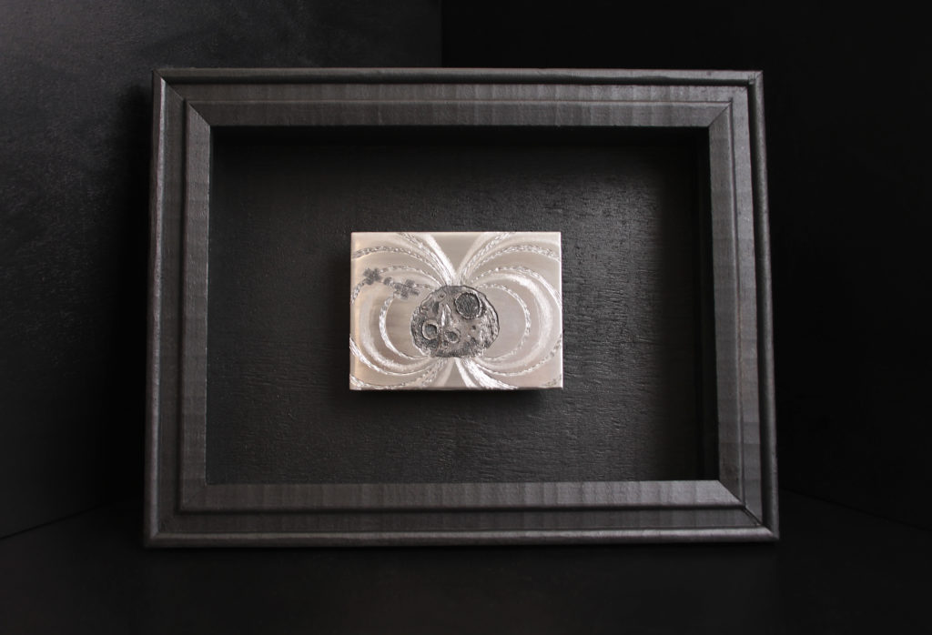 Here, a hand engraved steel plate depics an image of the Psyche asteroid with the Psyche spacecraft and radiating magnetic field. The plate is mounted on a black shadowbox frame.
