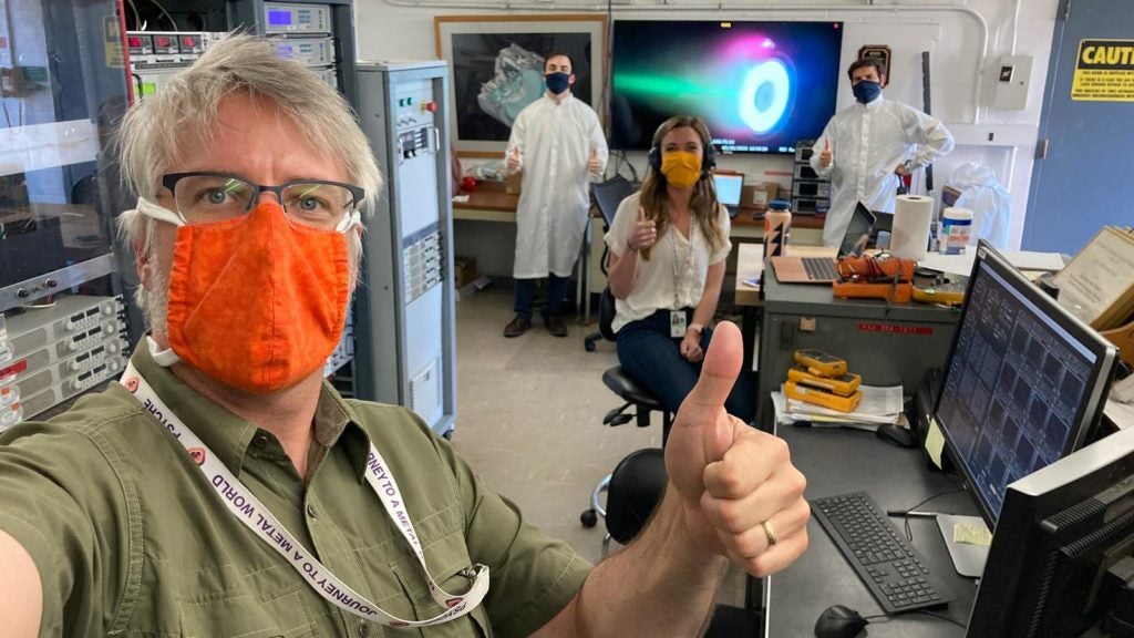 Scientist in a lab wearing masks while holding their thumbs up.