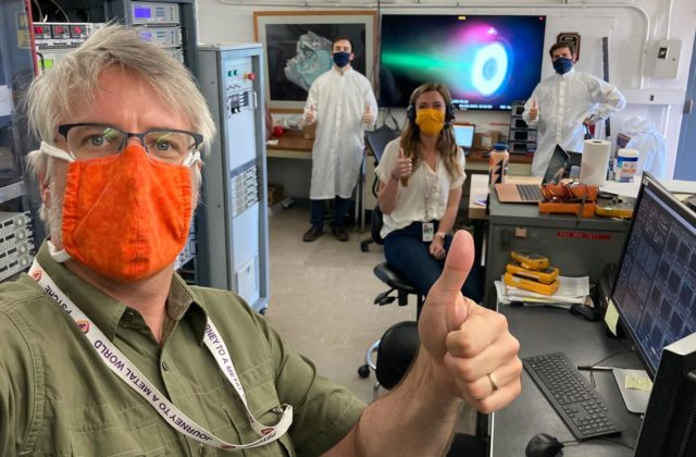 Scientist in a lab wearing masks while holding their thumbs up.