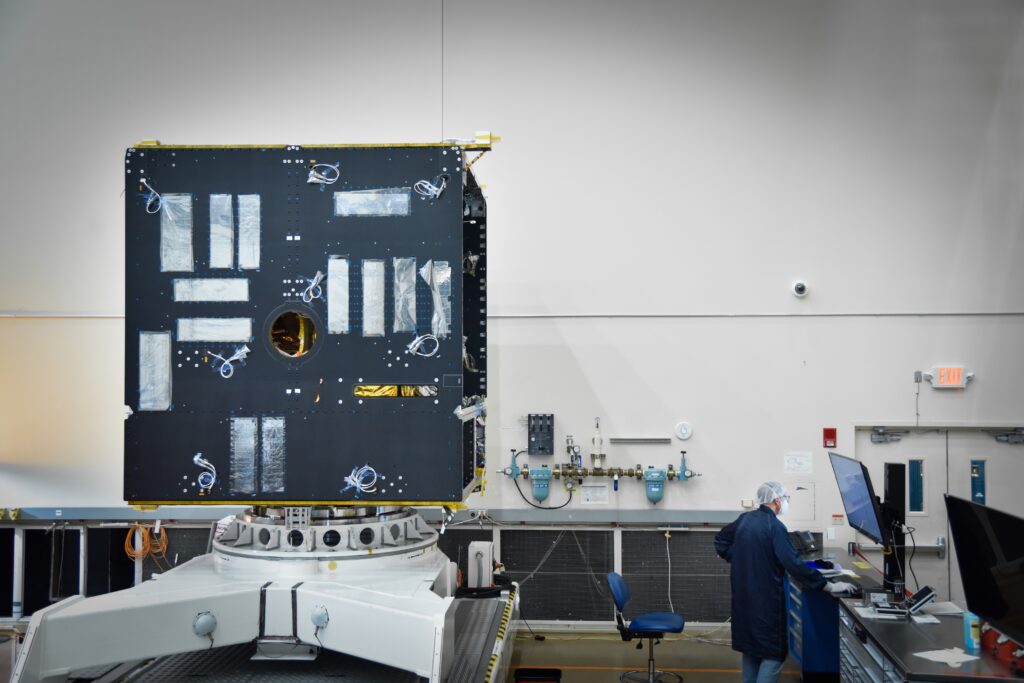 The body of the Psyche spacecraft is in progress. This image shows a black box with many wires sticking out of it and an engineer standing nearby.