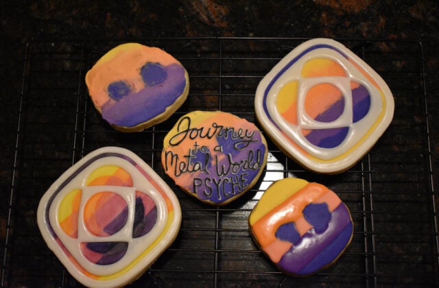 An asteroid-shaped cookie of the Psyche mission badge with black lettering that says, 