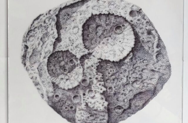 Black ink dots on plexiglass build up the form of Psyche. There are two major craters, a series of rifts and the surface appears pockmarked with small craters.