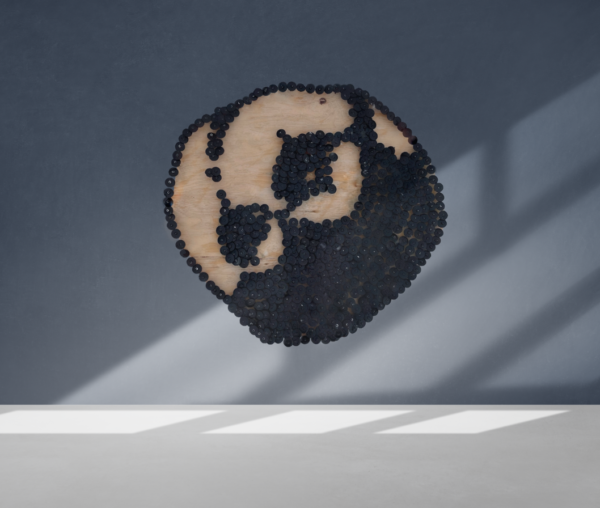 A sculpture of the Psyche asteroid hangs on a wall blue wall. The sculpture is made out of wood and black circular nail caps, which form two large craters. The nail caps also form Psyche's ridges and shadows.