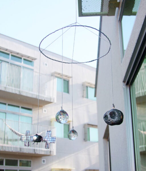 This is a hanging mobile made from wire, with clay pieces of Psyche and the satellite hanging by chains. They are painted in a shiny metallic paint that shimmers in the sun and are hanging with two sun catcher crystals.