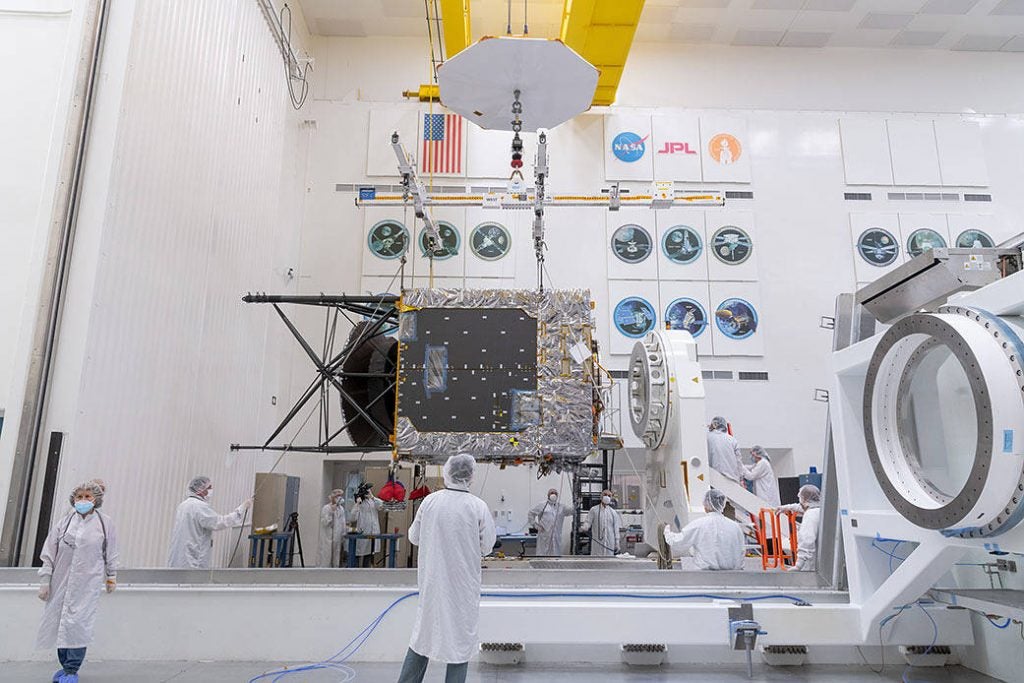 This image is of the main body of the spacecraft (the bus) in a factory space surrounded by engineers.