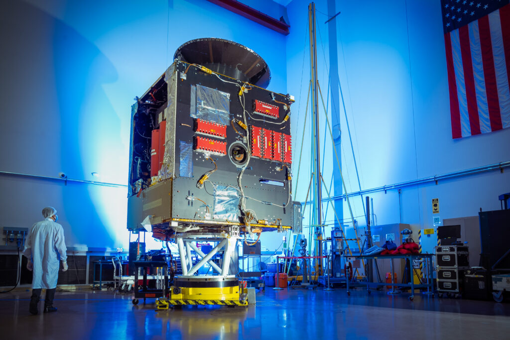 This image is of the main body of the spacecraft (the bus) in a factory space with a technician standing nearby.