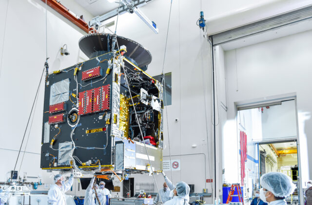 This image is of the main body of the spacecraft (the bus) in a factory space with technicians working.